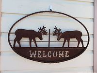 Front view of oval metal sign showing moose silhouettes and word Welcome