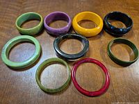 Nine assorted colored bangle bracelets displayed on wooden surface