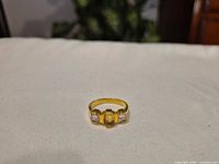 front view of gold-tone ring showing center yellow stone and side clear stones