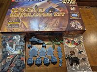 Lot overview showing Droid Developer Kit box, bags of LEGO pieces, Dinobloks Stegosaurus parts, and loose accessories