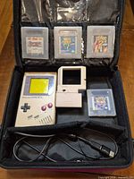 Open carrying case showing console, four game cartridges, clip-on light, link cable