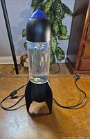 Full view of lamp unplugged on table showing black base, blue top, clear reservoir