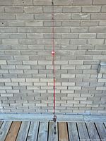 Full length of red fishing rod with reel attached