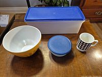 Group shot of all four items: rectangular Tupperware container with lid, round container with lid, yellow mixing bowl, checkered mug