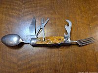 multi-tool fully opened: spoon, knife, scissors, bottle opener, can opener, fork visible