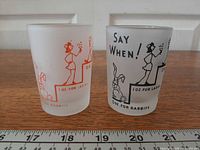 Front view of both frosted shot glasses showing red and black designs and ounce markings