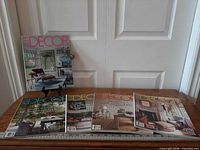 Five Elle Decoration magazines displayed on wooden surface, one standing, four laid flat