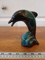 Front view of glazed ceramic dolphin on wave base with ruler for scale