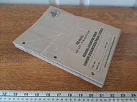 Stack of eight taupe exercise books showing covers and three-hole punches