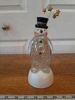Full view of Hallmark Merry Magic snowman snow globe on ruler showing height