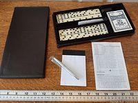 Open case showing domino tiles, playing cards, pen, notepad and instructions on table