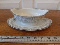 Side view of Noritake Oxford gravy boat on attached underplate with ruler for scale