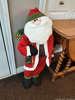 Full view of plush standing Santa figure beside small table
