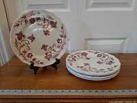 Stack of six red Windsong dinner plates beside single upright plate with ruler for scale