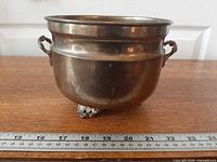 Front view of brass planter showing bowl shape, side handles, and decorative feet with ruler for scale
