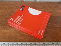 Stack of ten red Media exercise books showing front covers and ruler for scale