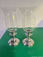 Pair of etched glass hurricane candle holders with silver bases displayed side by side