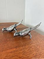 Two silver-tone pheasant figurines on table