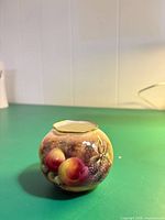 Front view of small round vase showing fruit design and overall form