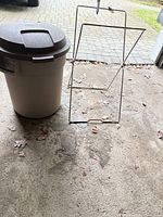 Trash can with lid beside metal rack on garage floor