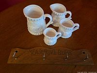 set of four measuring cup pitchers with wooden rack