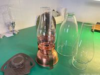 Lamp with attached chimney, two spare chimneys, metal trivet on tabletop