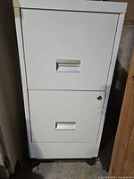 Front view of white two-drawer metal filing cabinet showing recessed handles and lock