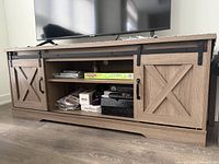 Front view of media console showing barn doors, open center shelving, TV on top