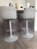 Rear view of both bar stools showing light gray faux leather seats and metal pedestal bases