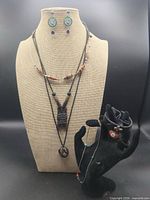 Bust displaying three necklaces and earrings; black hand shows bracelets and additional necklace