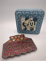 Front view of Mickey Mouse tin box and Coca-Cola trivet