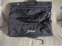 Front view of folded Titleist garment bag showing logo, exterior pocket, carry handle, hanging hook