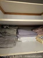 Stacked folded linens on shelf: grey and lavender sets visible
