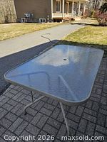 Full view of rectangular glass table on patio showing umbrella hole and legs