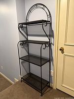 Full view of black wrought iron baker's rack against wall