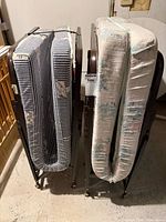 Two folded rollaway beds side by side showing mattress patterns and casters