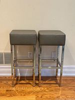 Front view of both stools showing chrome frames and grey faux leather seats