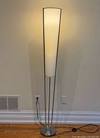 Full view of floor lamp illuminated showing base, rods, shade, cord and switch