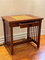 Three-quarter view of oak games table showing checkerboard top, one drawer open, slat sides, stretcher base