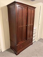 Front view of closed armoire showing paneled doors and drawer