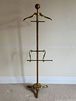 Full view of brass valet stand showing hanger, tray, pant rack, base