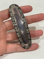 Front view showing oval shape, silver surface, spiral wire border