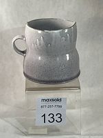Front view of speckled grey glazed mug on clear riser