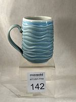 Front view of turquoise wave-textured mug on stand