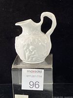 Front view of white porcelain miniature wine jug on stand