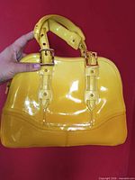 Front view of glossy yellow handbag with handles and buckle detailing
