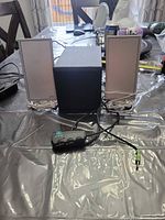 Two silver front satellite speakers, black cube subwoofer, inline control pod with cables and 3.5 mm plug