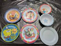 All eight children’s plates and bowls laid out showing character graphics and patterns