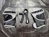 Hand grip strengthener centered between pair of fingerless gloves displayed on surface