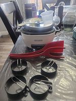 Entire lot showing rice cooker with lid, measuring cup, rice paddle, red tong utensil and four egg rings